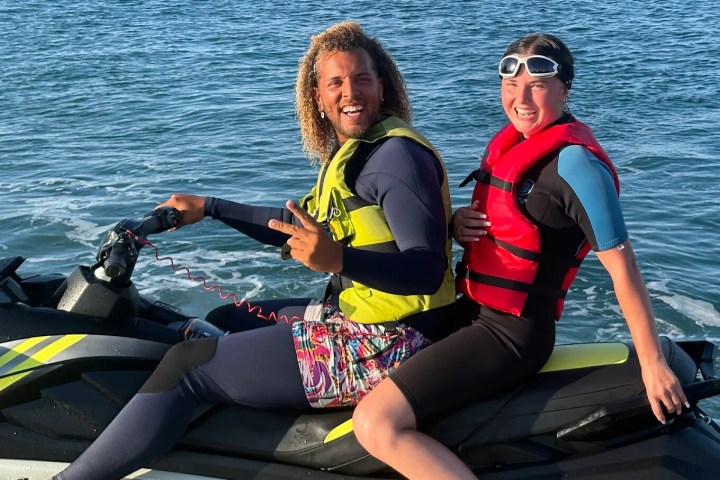 Two people in life vests riding a jet ski on the ocean, both smiling.